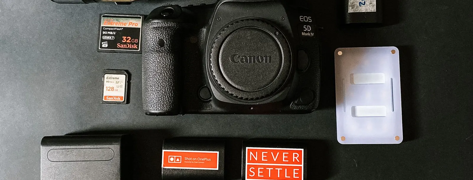 A photographer's kit — body, lenses, batteries and cards — laid out flat on a black surface.
