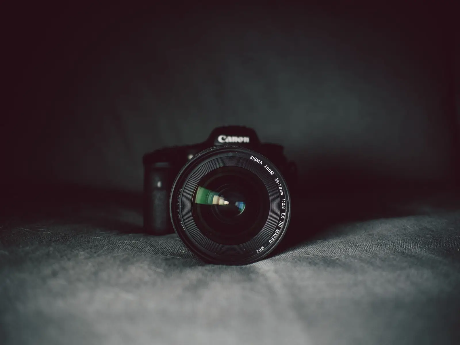 A camera body and lens on a dark surface, lit low-key.